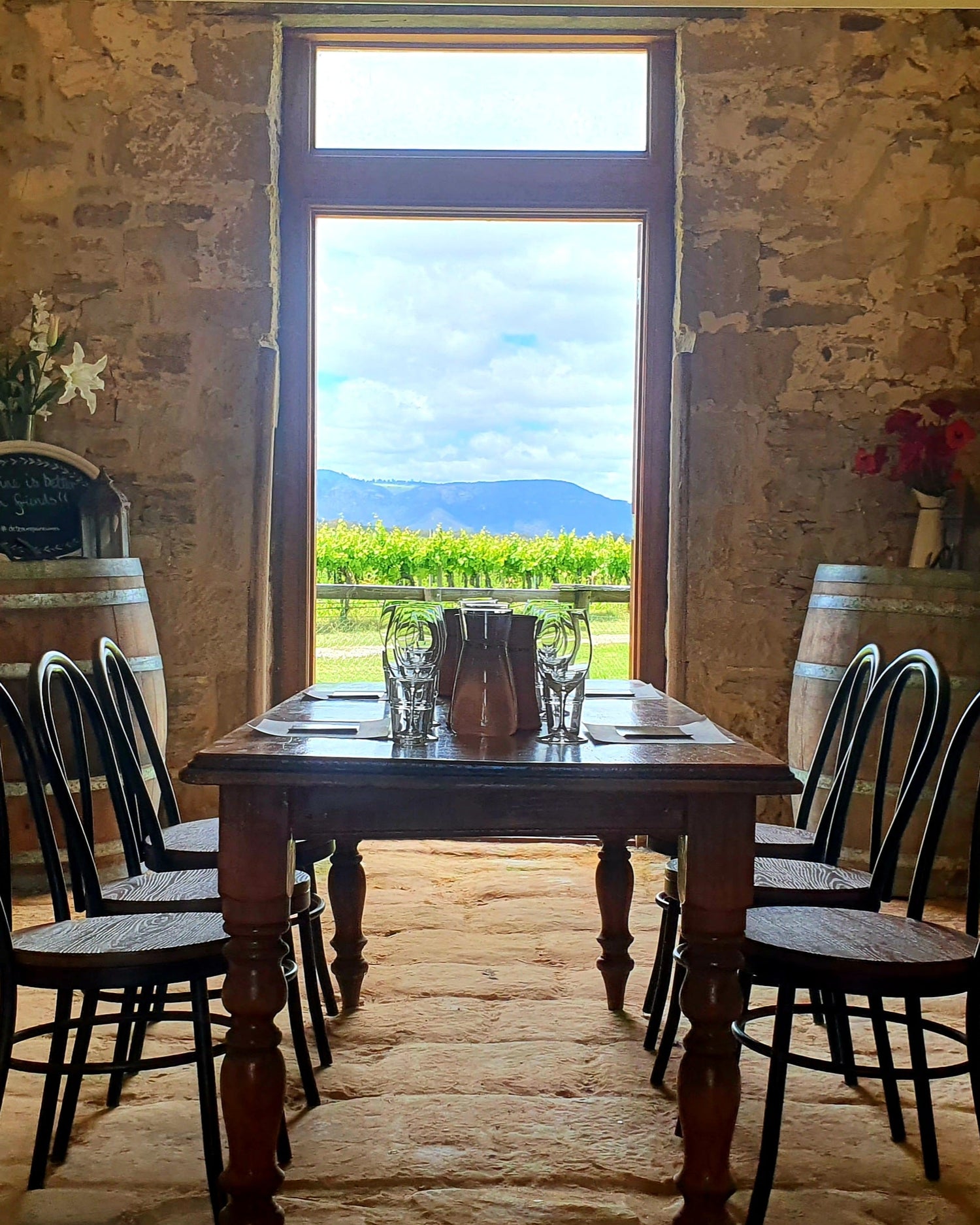 Dining area with wooden table and chairs in a rustic setting with a view of vineyards.